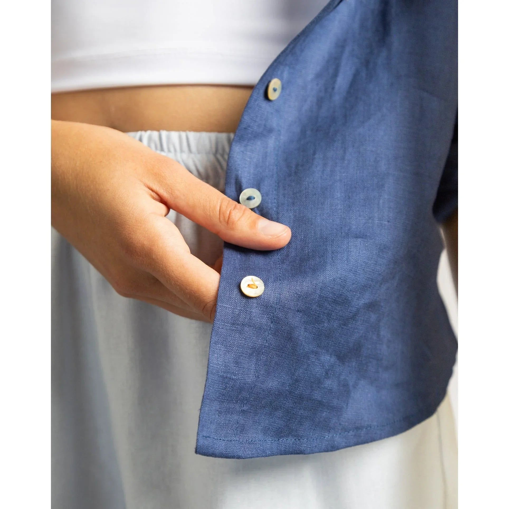 Close-up of a person buttoning a blue shirt with a blurred background